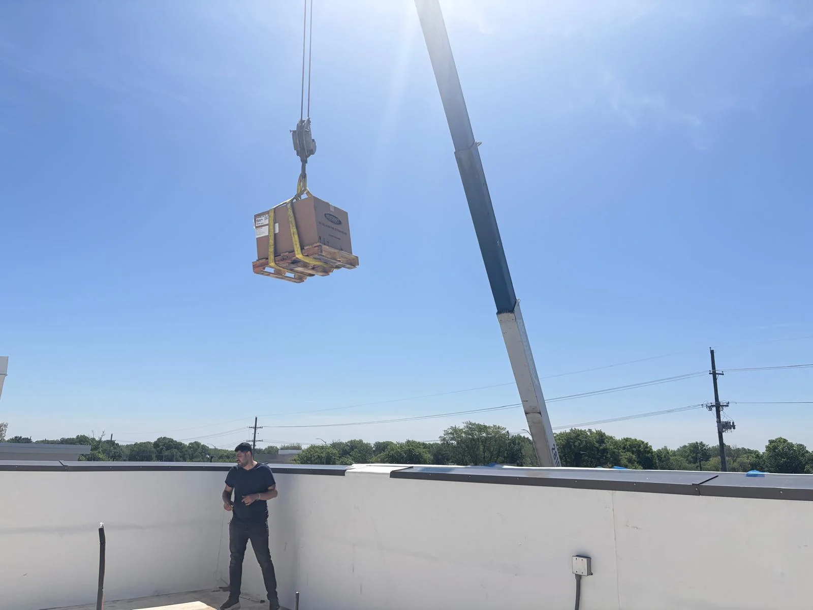 Crane lifting boxed commercial equipment onto roof